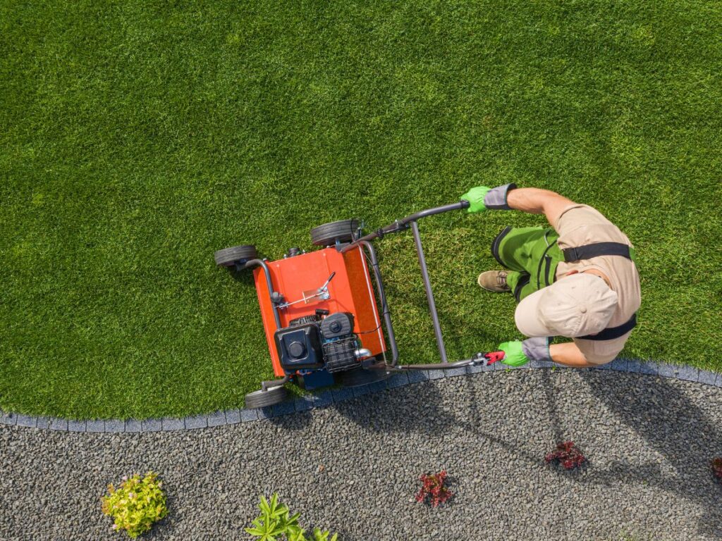 Lawn worker mowing a neatly edged lawn from above.